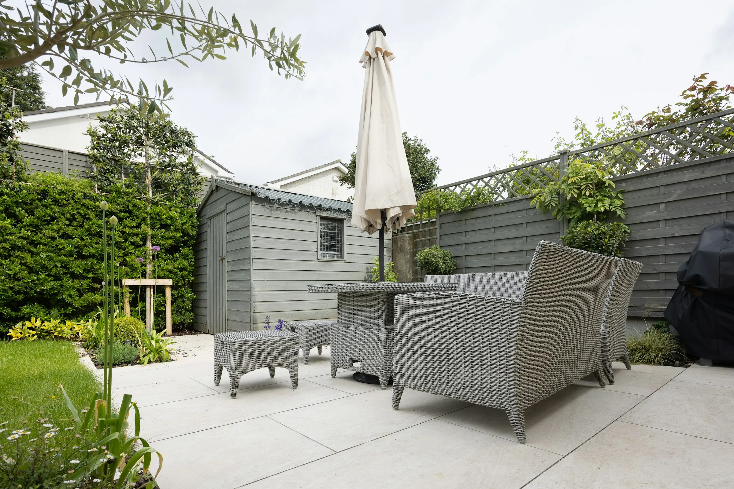 Pale porcelain patio with garden furniture beside a lawn