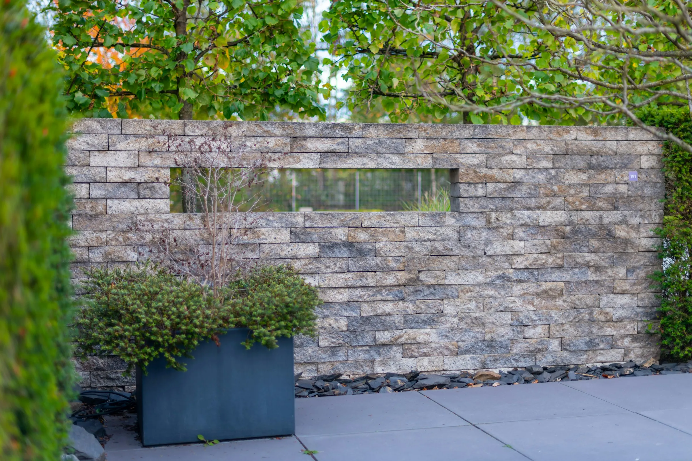 Stone feature wall with a slot window and a planter in front